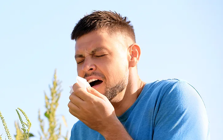 Ein Mann nießt mit einer Blüte in der Hand in ein Taschentuch in der Anderen