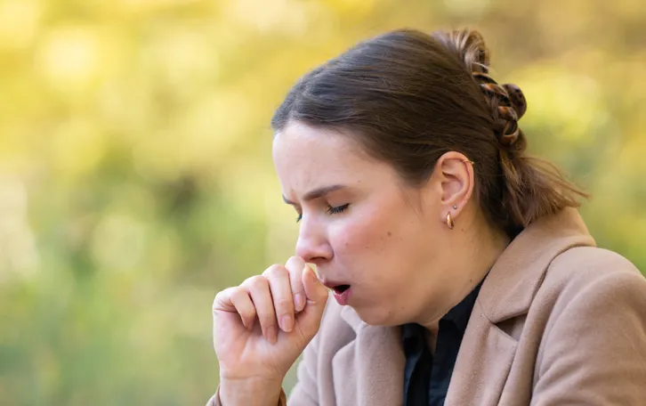 Eine Frau hustet sich in der Natur mit Mantel an in die Hand