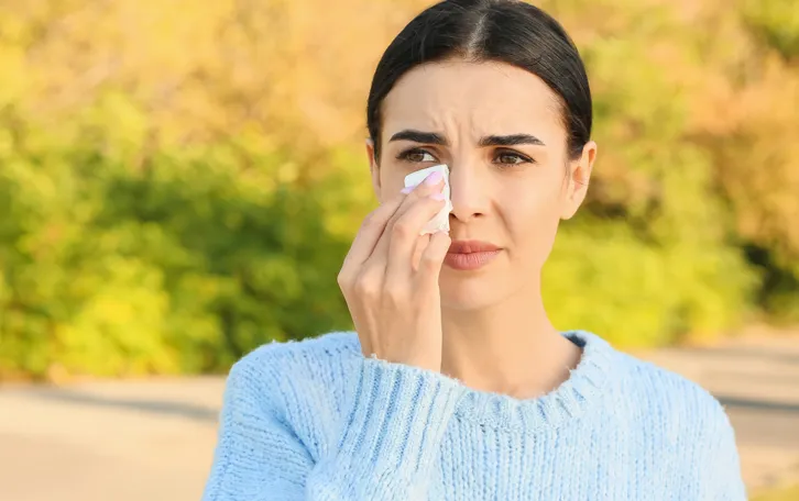 Eine Frau wischt mit einem Taschentuch im Freien unter ihrem rechten Auge lang